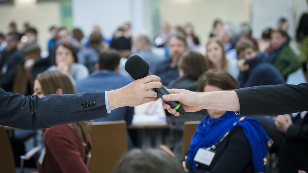 Eine Person übergibt ein Mikrophone einer anderen Person 
