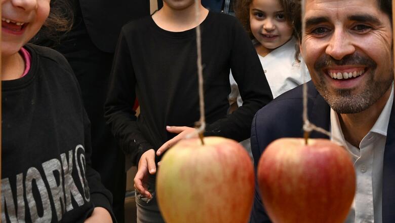 Sven Teuber, Bilcungsminister Rheinland-Pfalz, bei einem MINT-Experiment mit Äpfeln. Mehrere Grunsschulkinder schauen zu
